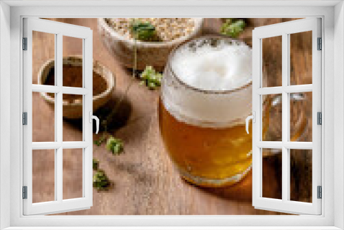 Fototapeta Naklejka Na Ścianę Okno 3D - Classic glass mug of fresh cold foamy lager beer with green hop cones, wheat grain and red fermented malt in ceramic bowls behind over wooden texture background. Copy space