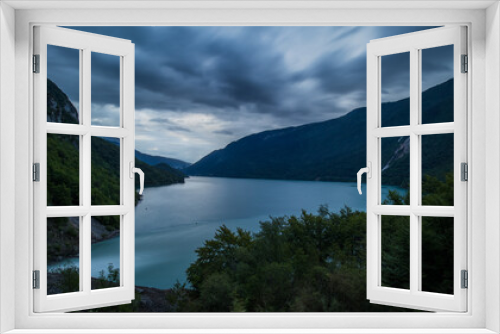 Fototapeta Naklejka Na Ścianę Okno 3D - Evening panorama of Molveno lake with visible overflow waterfall of the power plant with wild white water falling into the lake. Long exposure of clouds