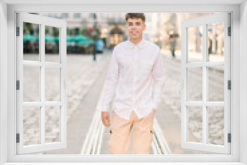 Summer day, walk in the city concept. Front view of young stylish Caucasian man dressed in white shirt and beige pants, standing on city street