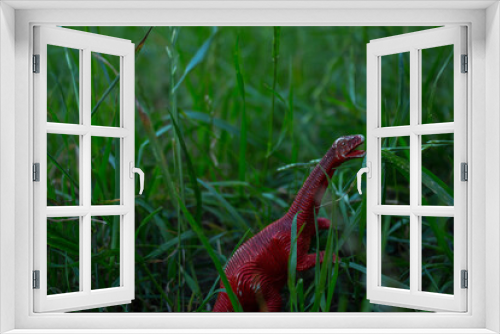 Fototapeta Naklejka Na Ścianę Okno 3D - a toy dinosaur stands among the green grass