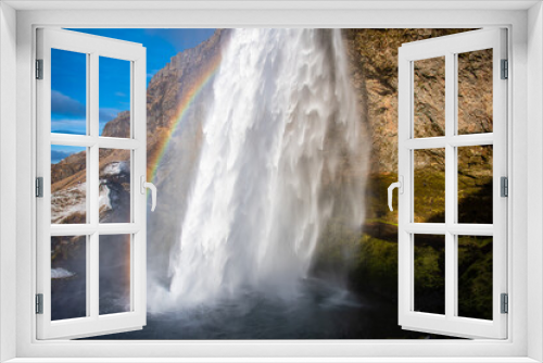 Fototapeta Naklejka Na Ścianę Okno 3D - Waterfall from a cliff with a rainbow and mist in Iceland. The area behind the waterfall can be seen.