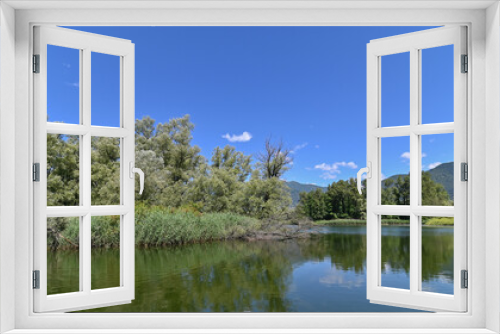 Fototapeta Naklejka Na Ścianę Okno 3D - Panorama di un bel lago circondato da una grande palude con alberi verdi e cielo blu