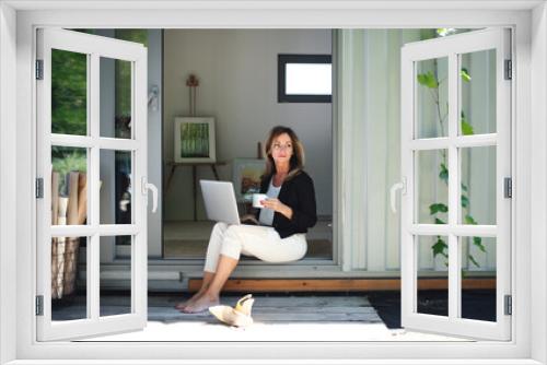 Mature woman working in home office in container house in backyard.