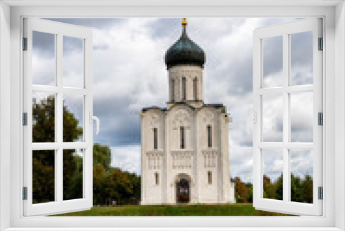 Fototapeta Naklejka Na Ścianę Okno 3D - snow-white stone old church against the background of a green meadow and lake before a summer thunderstorm