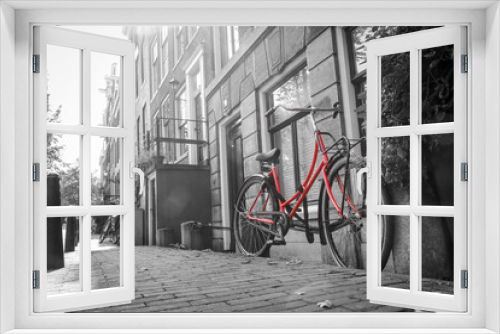 Fototapeta Naklejka Na Ścianę Okno 3D - A picture of a lonely red bike on the street by the channel in Amsterdam. The background is black and white. 