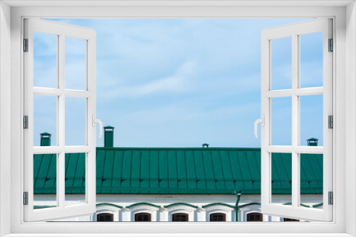 Fototapeta Naklejka Na Ścianę Okno 3D - Green metal roof on a white brick building with metal chimneys against a blue sky