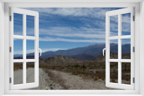 Fototapeta Naklejka Na Ścianę Okno 3D - Desert route across the death valley. View of the dirt road, desert and mountains under a beautiful blue sky with clouds.