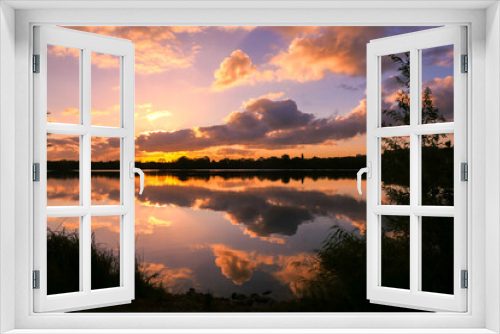 Fototapeta Naklejka Na Ścianę Okno 3D - Amazing sunrise in rural scene. Symmetry of the sky in a lake at sunset. Clouds reflecting on the water. Quiet relaxing scene with a beautiful colorful cumulonimbus. Silhouette of vegetations.