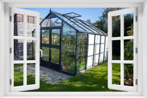 Fototapeta Naklejka Na Ścianę Okno 3D - greenhouse stands next to a garage in a garden, the sun is shining and the sky is blue