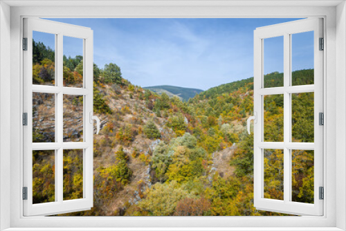Fototapeta Naklejka Na Ścianę Okno 3D - Amazing fall colors of the trees in the forest in a valley, surrounded by hills and distant mountain peak under a blue sky