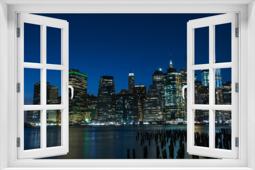 Fototapeta Naklejka Na Ścianę Okno 3D - Night photo of glowing skyscrapers and a view of Manhattan Bay. Long duration. Panoramic photo. The splendor of the city at night.