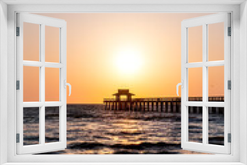 Fototapeta Naklejka Na Ścianę Okno 3D - Naples, Florida vertical view of red yellow and orange sunset in gulf of Mexico coast with sun path by pier wooden jetty with horizon and dark blue ocean waves