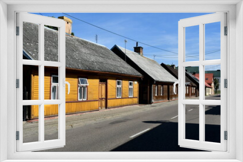 Fototapeta Naklejka Na Ścianę Okno 3D - View of a street of a Polish village or cottage with a set of old historic abandoned houses or huts made out of planks, logs, and boards with angled roofs and brick chimneys seen on a sunny summer day