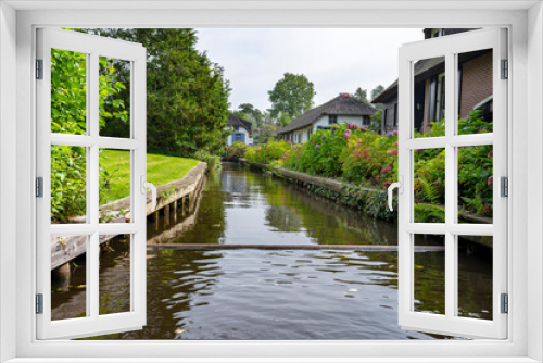 Fototapeta Naklejka Na Ścianę Okno 3D - A canal flowing between buildings in a famous village in the Netherlands, visible trees and flowers in the gardens.