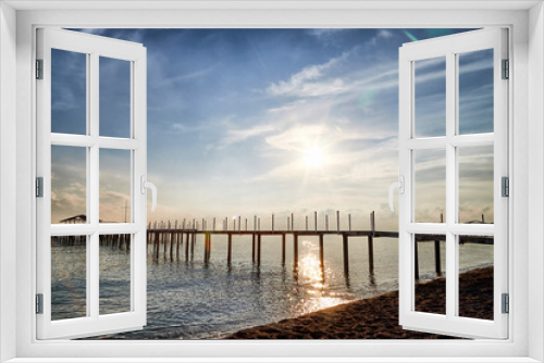 Fototapeta Naklejka Na Ścianę Okno 3D - View from sand beach to water of sea, waves and pier in a nice day or evening with blues sky, bright sun and white clouds. The concept of a holiday on the sea or ocean in the South.