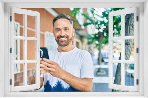 Middle age handsome man smiling happy using smartphone at the city.