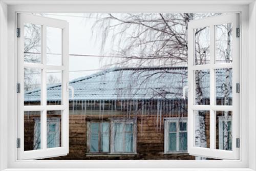 Fototapeta Naklejka Na Ścianę Okno 3D - Icicles hang from  roof of  building. Old wooden house in winter weather. . White birches at home