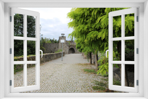 Fototapeta Naklejka Na Ścianę Okno 3D - Calle empedrada de características medievales con arboles a los costados y un arco de piedra al dinal del camino, una lampara en el sendero