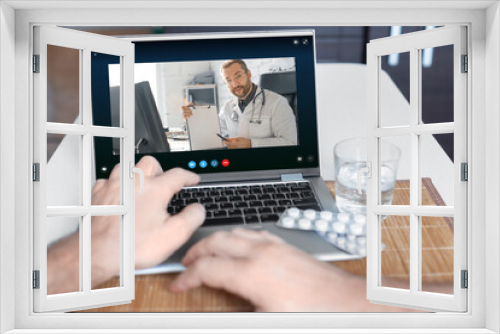 Close-up view of a patient's hand in front of a laptop during an online consultation with a doctor.