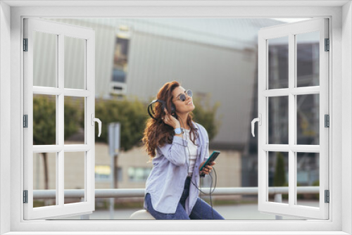 Young pretty student girl, waiting for a taxi car, and listening to music from the phone on big headphones