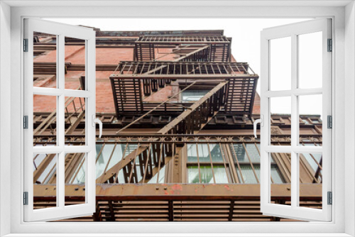 Fototapeta Naklejka Na Ścianę Okno 3D - Low Angle View of Typical Apartments with Fire Escape Ladders in Manhattan, New York City, USA