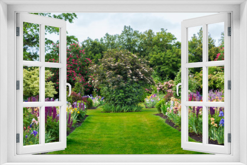 Fototapeta Naklejka Na Ścianę Okno 3D - An English Style Garden Path with Mowed Lawn, Mixed Flower Beds - Daytime, with Pale Blue Sky