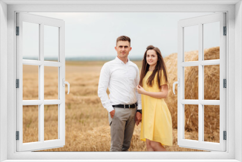 Photo of joyful couple man and woman walking through golden field with bunch of haystacks and hugging together during sunny day