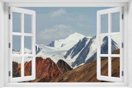 Fototapeta Naklejka Na Ścianę Okno 3D - Minimalist beautiful alpine landscape with huge snowy mountain behind vivid pointed red craggy wall. Big glacier under blue sky. Atmospheric colorful highland scenery with giant red orange brown rock.