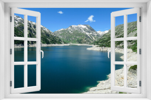 Fototapeta Naklejka Na Ścianę Okno 3D - Dam in Austrian Alps. The artificial lake stretches over a vast territory, shining with navy blue color. The dam is surrounded by high mountains. In the back there is a glacier. Controlling the nature