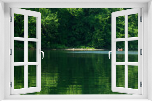 Fototapeta Naklejka Na Ścianę Okno 3D - Majestic vertical nature background woth two tiny kayakers in the distance. Green foliage reflected in river water for beautiful tranquil effect in bright sunshine with copy space.