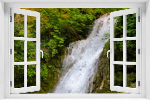 Fototapeta Naklejka Na Ścianę Okno 3D - View of a small waterfall surrounded by greenery and trees.