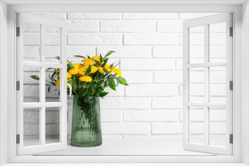Fototapeta Naklejka Na Ścianę Okno 3D - Bouquet of beautiful yellow flowers in glass vase on white wooden table near brick wall. Space for text