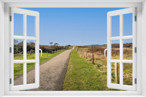 Fototapeta Naklejka Na Ścianę Okno 3D - A seemingly endless cycling and walking path through the Dutch dunes on the North Sea near the village of Ouddorp, South Holland province. It's a sunny day in winter and there is no one in the area.