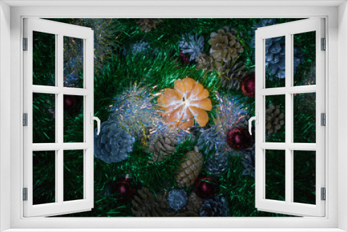 Fototapeta Naklejka Na Ścianę Okno 3D - Peeled fresh bright mandarin amidst green and shimmering tinsel with cones painted in silver and gold.
