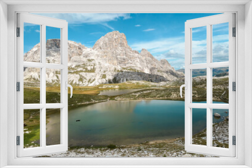 Fototapeta Naklejka Na Ścianę Okno 3D - A small, navy blue lake at the bottom of the valley in Italian Alps. The lake is surrounded by high and steep peaks. The slopes are lush green. The sky is full of soft clouds. Raw landscape. Remedy