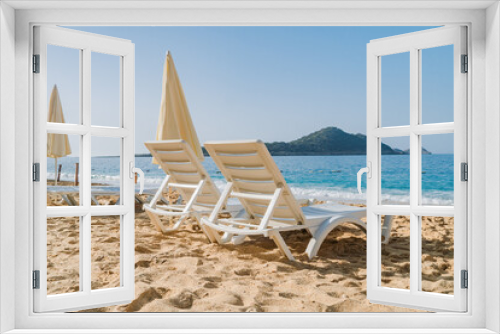 Fototapeta Naklejka Na Ścianę Okno 3D - Empty Beach chairs and a yellow sun umbrella await tourists against the backdrop of the blue sea. Beautiful seashore beach resort.