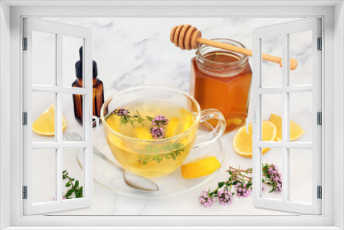Fototapeta Naklejka Na Ścianę Okno 3D - Healing thyme herb & lemon hot drink for cold and flu virus in a glass tea cup with honey and essential oil. Immune boosting medication, is anti bacterial, antiseptic and anti viral. On marble.