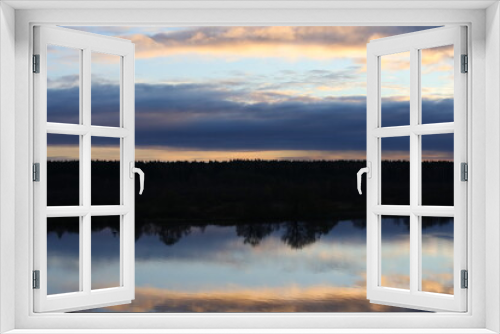 Fototapeta Naklejka Na Ścianę Okno 3D - Night landscape by the river with a black forest reflected in the blue water with clouds and a Golden strip of the horizon.Abstract natural image