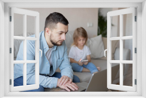 Father working from home with small child while in quarantine isolation during the Covid-19. Little girl looking on smartphone. 