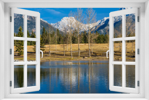 Fototapeta Naklejka Na Ścianę Okno 3D - Quarry Lake park lakeshore in late autumn season sunny day morning. Snow capped Mount Lady MacDonald, Grotto Mountain and withered trees reflect on the water surface. Canmore, Alberta, Canada.