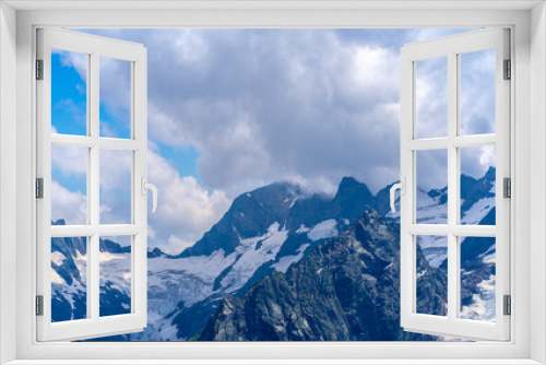 Fototapeta Naklejka Na Ścianę Okno 3D - Snowy mountain against cloudy sky. From below white clouds floating on blue sky over mountain ridge covered with snow on sunny day in nature