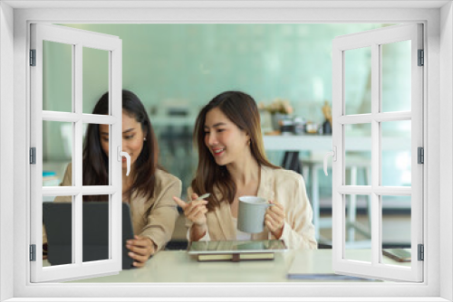 Two businesswomen working together in glass partition office room