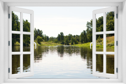 Fototapeta Naklejka Na Ścianę Okno 3D - River in summer on a sunny day, green grass and forest. Reflection in the water. Domestic tourism, ecotourism, unity with nature. Clean environment, protection. Water hiking and camping. Summertime.