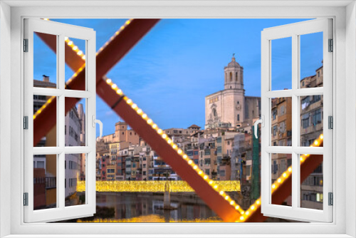 Fototapeta Naklejka Na Ścianę Okno 3D - Girona's urban cityscape skyline at dusk with famous gothic cathedral landmark and river houses reflected on a quiet river from red iron bridge