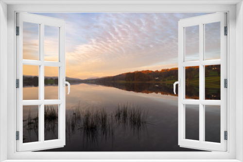Fototapeta Naklejka Na Ścianę Okno 3D - Peaceful dusk falls across Esthwaite Water with reflections in the water of buildings, trees and colourful clouds in a mackerel sky, Lake District, UK