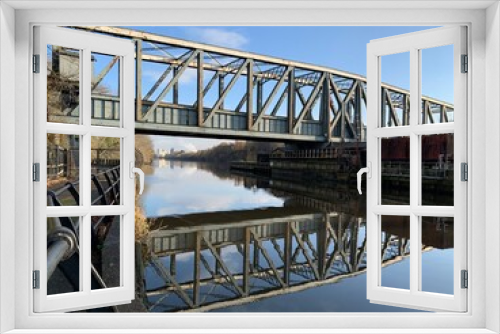 Fototapeta Naklejka Na Ścianę Okno 3D - Old metal bridge going over the Manchester ship canal with reflections in the water and a blue sky background. 