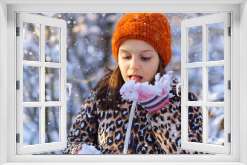 child girl eats snow and having fun in the winter forest, bright sunlight and shadows on the snow, beautiful nature