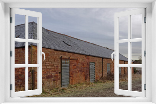 Fototapeta Naklejka Na Ścianę Okno 3D - Part of an old Agricultural Farm Store Complex with metal shutter doors built into the red Stone Building on an abandoned Golf Course near Arbroath.