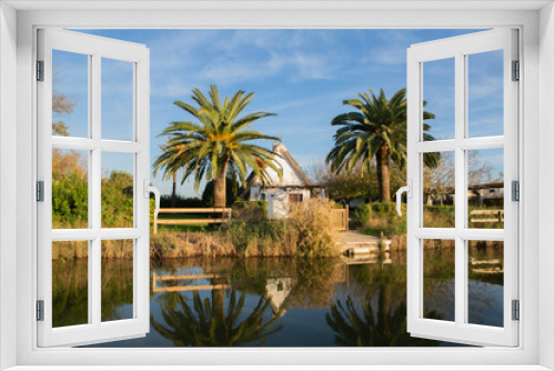 Fototapeta Naklejka Na Ścianę Okno 3D - View of a traditional Valencian house on the edge of a lagoon in a natural park among palm trees