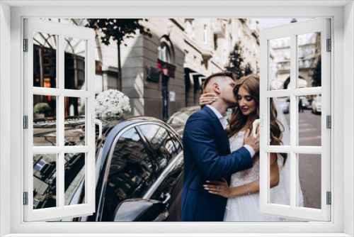 A romantic walk of the bride and groom through the city streets. Newlyweds on the background of a black car.